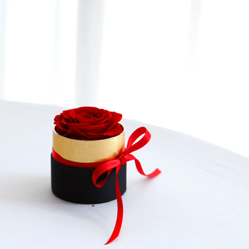 Small round black box with a red rose and a red ribbon on a white background