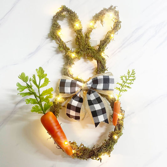 Decorative wreath shaped like a bunny with lights, carrots, and a checkered bow Easter decoration