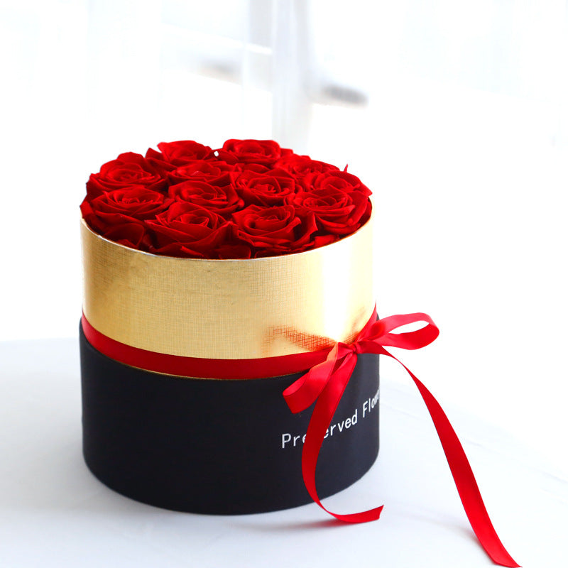 Round black box with gold interior containing red roses on a white background