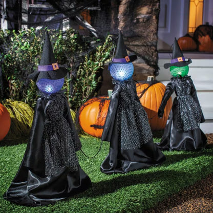 Three witch figurines with colorful LED lights on their heads in a Halloween setting.